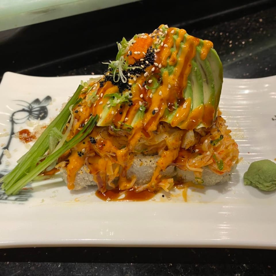 Yama Fuji's volcano roll, topped with avocado, spicy sauce, roe, sesame seeds, and green onions.