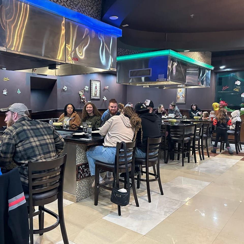 Diners seated at hibachi tables under stainless steel hoods with blue and green lighting at Yama Fuji.