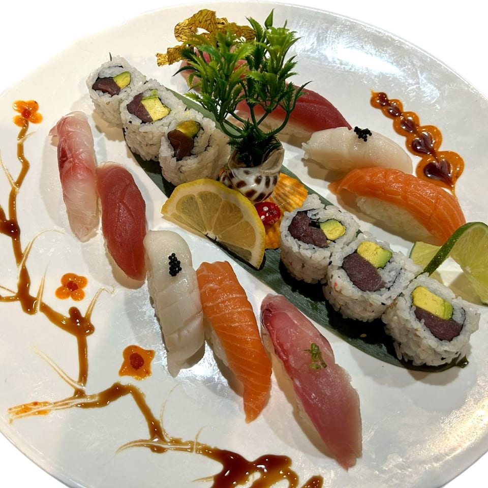 A white plate of Yama Fuji sushi and sashimi, garnished with lemon, lime, and sauce.